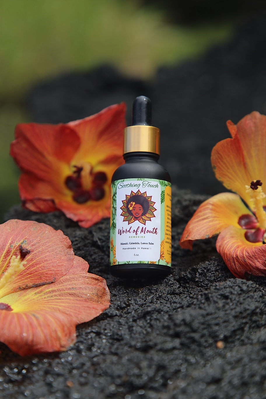 Soothng Touch Tincture bottle sitting on lava rock with flowers around it.